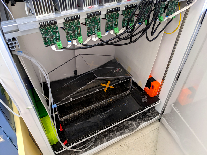 Clear box sits in a growth chamber. Many wires come from the chamber