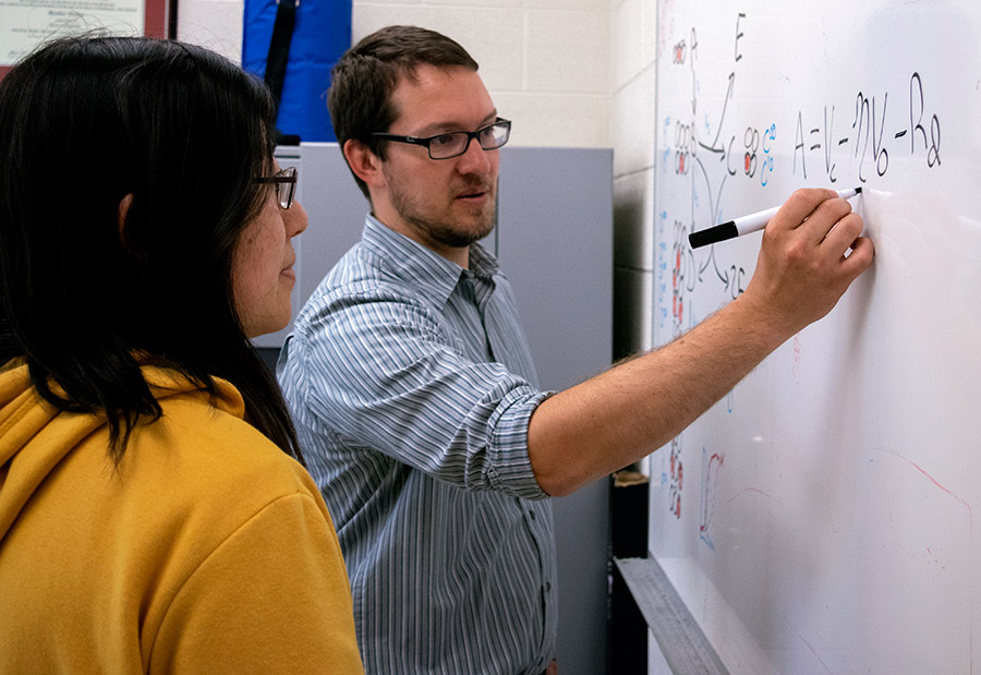 Two scientists discuss an equation on the whiteboard.